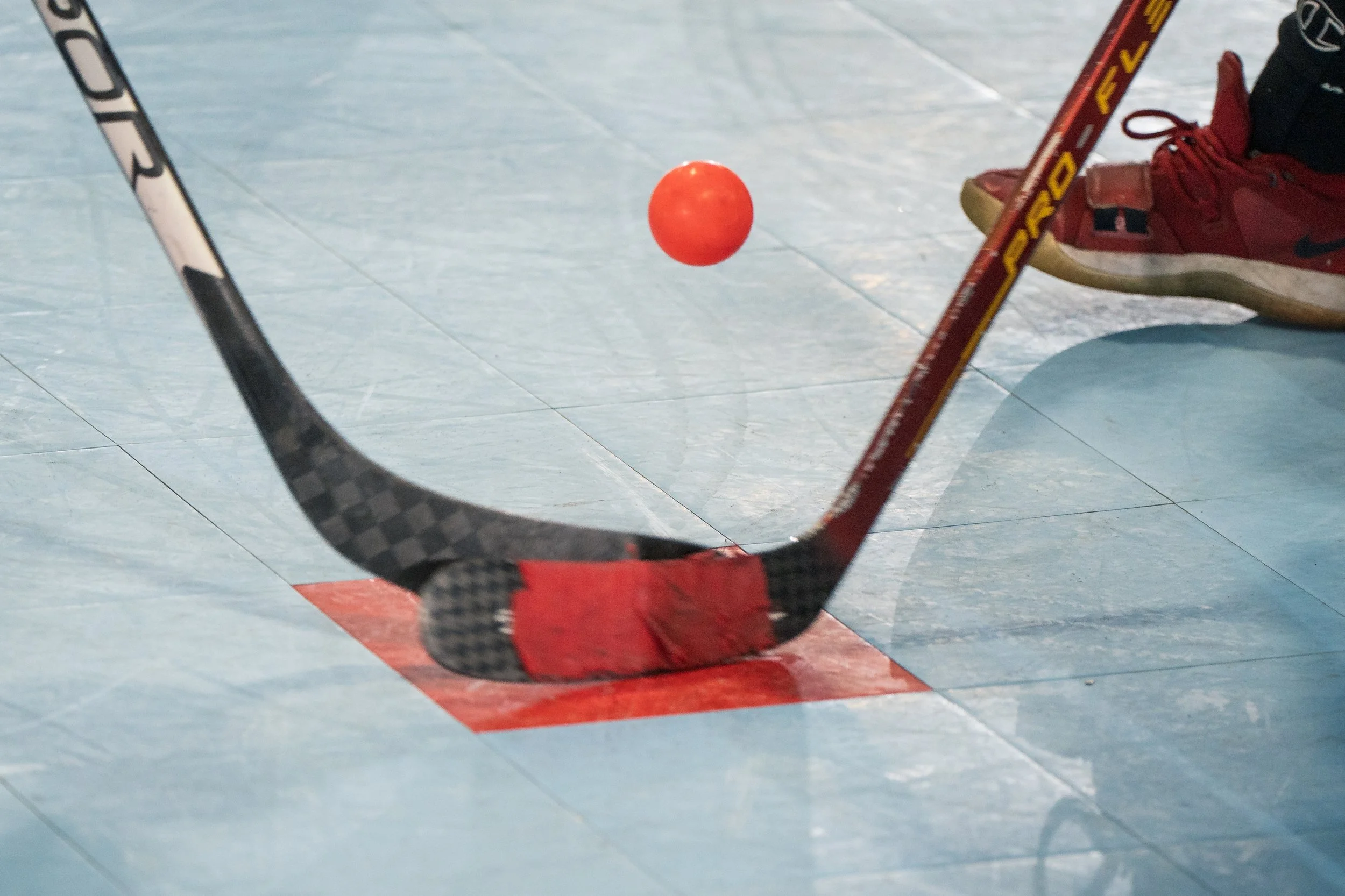 Two ball hockey players face off over an orange ball